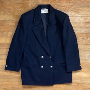 May include: A navy blue double-breasted blazer with silver buttons. The blazer has a classic style and is made of a high-quality fabric.