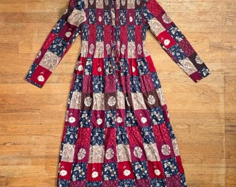 Könnte beinhalten: Ein langärmeliges Midikleid mit einem Patchwork-Muster aus Quadraten in Rot-, Marineblau- und Beigetönen. Das Kleidungsstück hat einen Rundhalsausschnitt, eine durchgehende Knopfleiste vorne, ein tailliertes Oberteil und einen ausgestellten Rock.