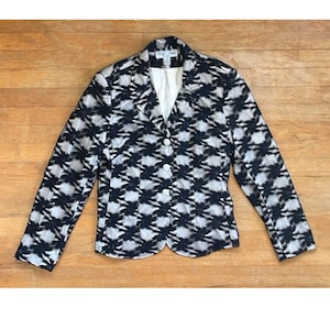 May include: A black and white patterned blazer with a button closure. The blazer has a notched collar and long sleeves.