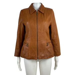 May include: A brown leather jacket with a zip fastening and two pockets on the front. The jacket has a collar and long sleeves.
