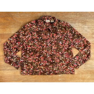 May include: A button-down shirt with a brown background and a pattern of red and white leaves. The long-sleeved shirt has a collar and buttons down the front. The shirt is made of a lightweight material.