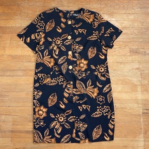 Puede incluir: Un vestido midi negro con estampado floral marrón. El vestido tiene un frente abotonado y mangas cortas.