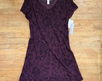 Könnte beinhalten: Ein pflaumenfarbenes Kleid mit V-Ausschnitt und kurzen Ärmeln. Das Kleid hat einen mehrschichtigen Rock und ein schwarzes Blumenmuster. Ein Etikett ist am Kleid befestigt. Das Kleid ist aus leichtem Stoff gefertigt.