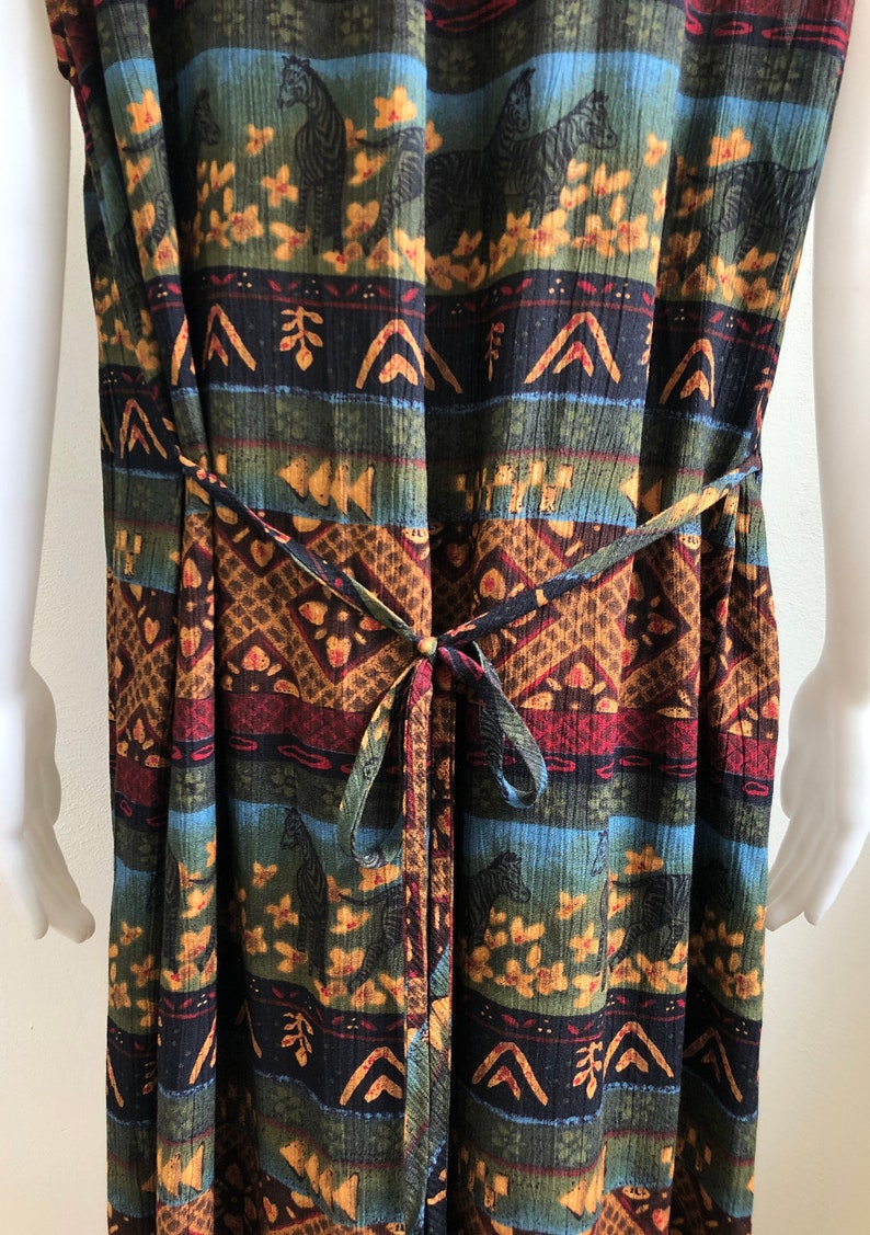 May include: A long, sleeveless dress with a colorful, tribal-inspired print featuring zebras and geometric patterns. The dress has a tie at the waist.