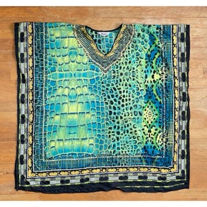 Puede incluir: Una túnica estampada y colorida con cuello en V. La parte superior presenta una mezcla de tonos azules, verdes y amarillos con un patrón de escamas de reptil. Los bordes están adornados con detalles negros y dorados, creando un aspecto vibrante.