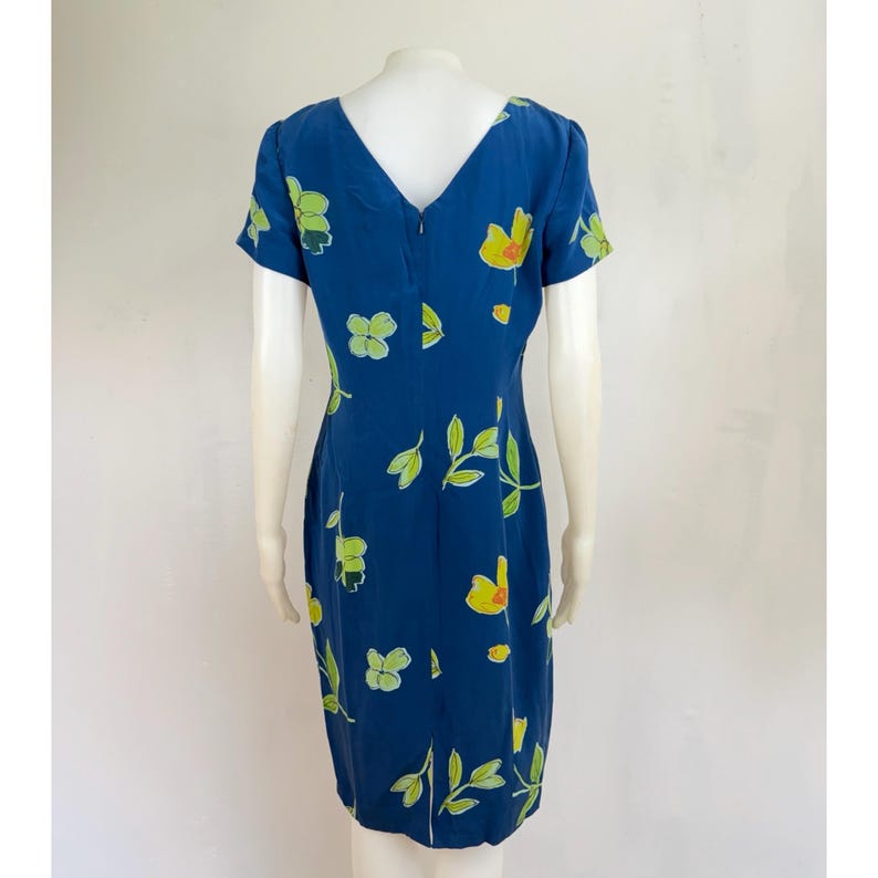 Puede incluir: Vestido azul marino con cuello en V y mangas cortas. El vestido est&aacute; adornado con un estampado floral con flores amarillas y verdes y hojas verdes. El vestido es hasta la rodilla y tiene cierre de cremallera en la espalda.