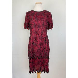 May include: A burgundy sequined dress with black floral embroidery. The dress has short sleeves and a fitted silhouette. The hemline is scalloped and features a layered design.