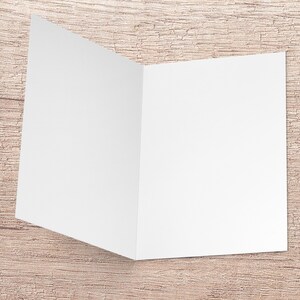 May include: A blank white card folded in half, ready for a message. The card is sitting on a light brown wooden surface.