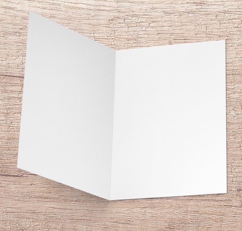 May include: A blank white card folded in half, ready for a message. The card is sitting on a light brown wooden surface.