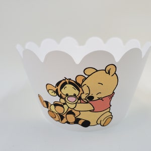 May include: White cupcake liner with a scalloped edge featuring a cartoon image of Winnie the Pooh and Tigger hugging.