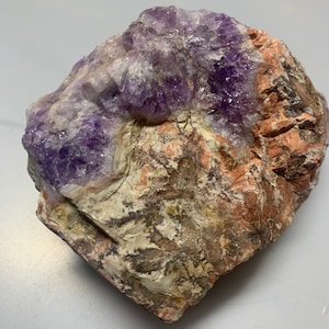 May include: A large, rough amethyst crystal cluster with purple and white crystals embedded in a matrix of brown, white, and pink rock.