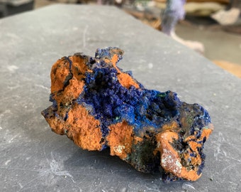May include: A rough, brown rock with blue and green azurite crystals. The rock has a natural, earthy texture.