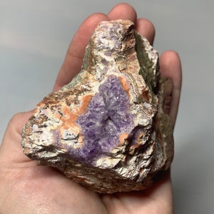 May include: A large, rough, purple amethyst geode with a white and orange agate exterior. The geode is partially open, revealing the purple amethyst crystals inside.