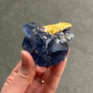 Pode incluir: Um cristal de fluorita azul com uma tampa de calcita amarela. O cristal tem uma textura áspera e natural e é um belo exemplo deste mineral.