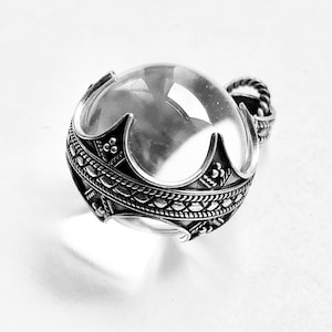 May include: A silver pendant featuring a clear glass orb encased in an intricate silver frame. The frame has a rope-like design and a decorative pattern.