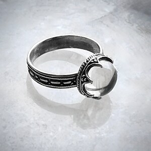 May include: A silver ring with a clear quartz stone set in a detailed, ornate design.