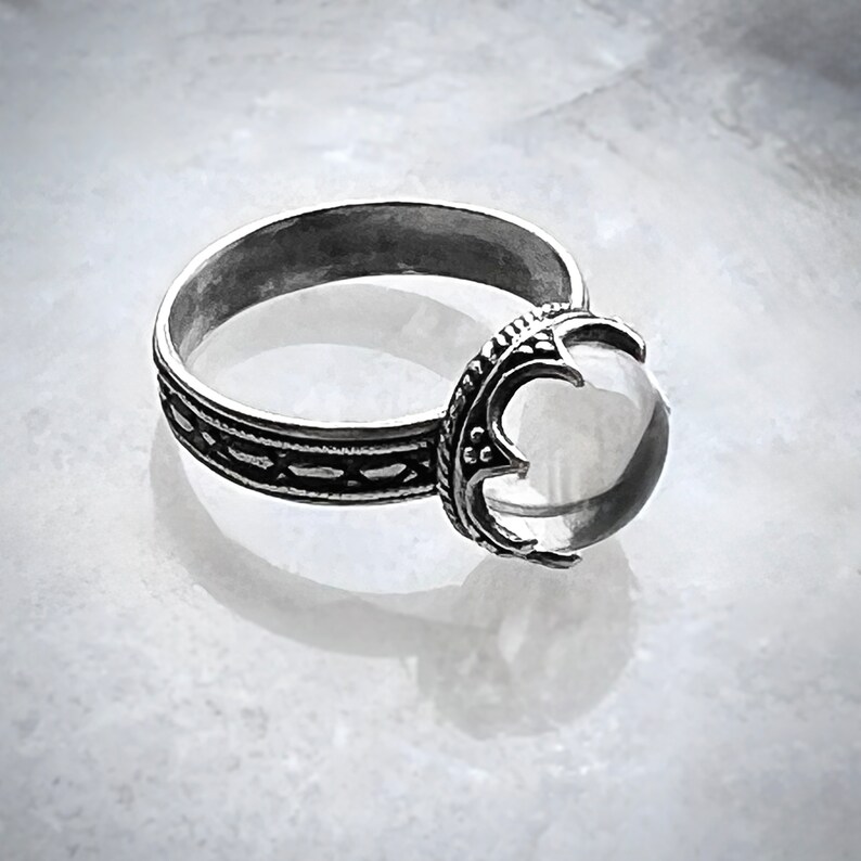May include: A silver ring with a clear quartz stone set in a detailed, ornate design.