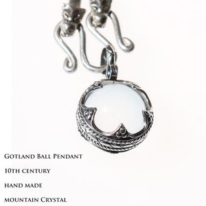 Puede incluir: Un colgante de bola de Gotland de plata con un cristal de roca blanco. El colgante est&aacute; en una cadena de plata con dos cierres de cabeza de drag&oacute;n. El colgante est&aacute; hecho a mano y data del siglo X. El texto "VIKING KRISTALL SUECIA" est&aacute; en la parte inferior de la imagen.