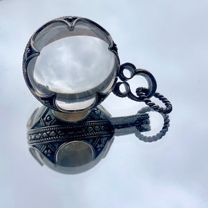 May include: A silver pendant featuring a large, clear crystal at its centre. The crystal is surrounded by intricate silver designs. The pendant is attached to a silver chain.