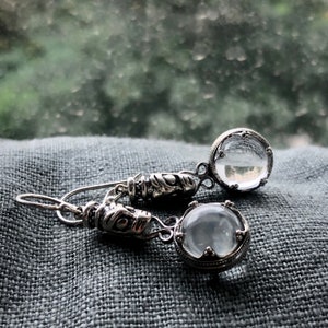 May include: A pair of silver earrings with clear glass stones. The stones are set in ornate silver frames.