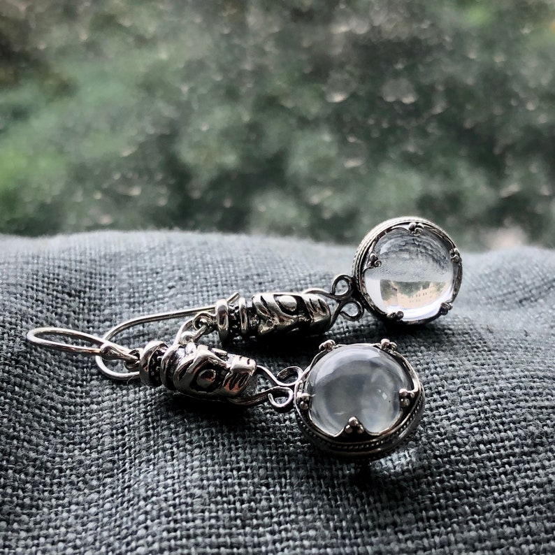May include: A pair of silver earrings with clear glass stones. The stones are set in ornate silver frames.