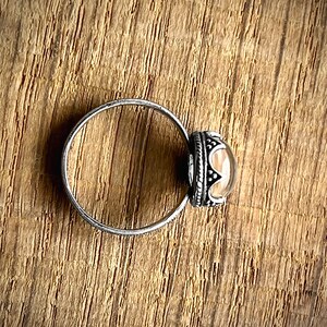 May include: A silver ring with a clear stone set in a silver bezel. The bezel is decorated with a detailed design.