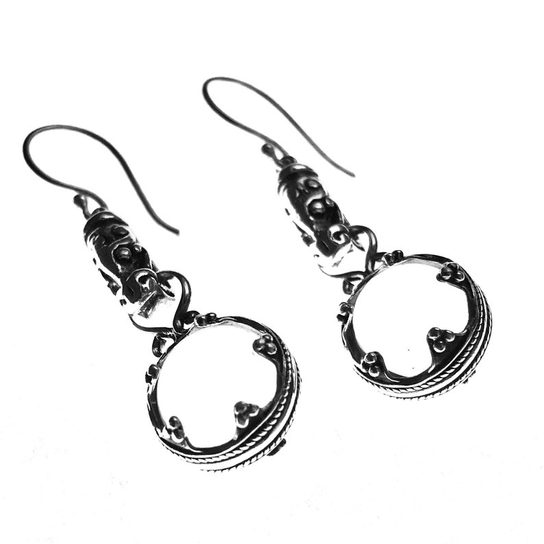 May include: A pair of silver dangle earrings with a round, open circle design. The earrings have a textured, ornate design and a hook closure.