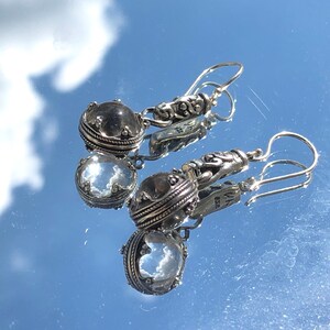 May include: A pair of silver dangle earrings with clear crystal stones. The earrings have a detailed design with a silver filigree and a small silver bead at the top of the crystal.