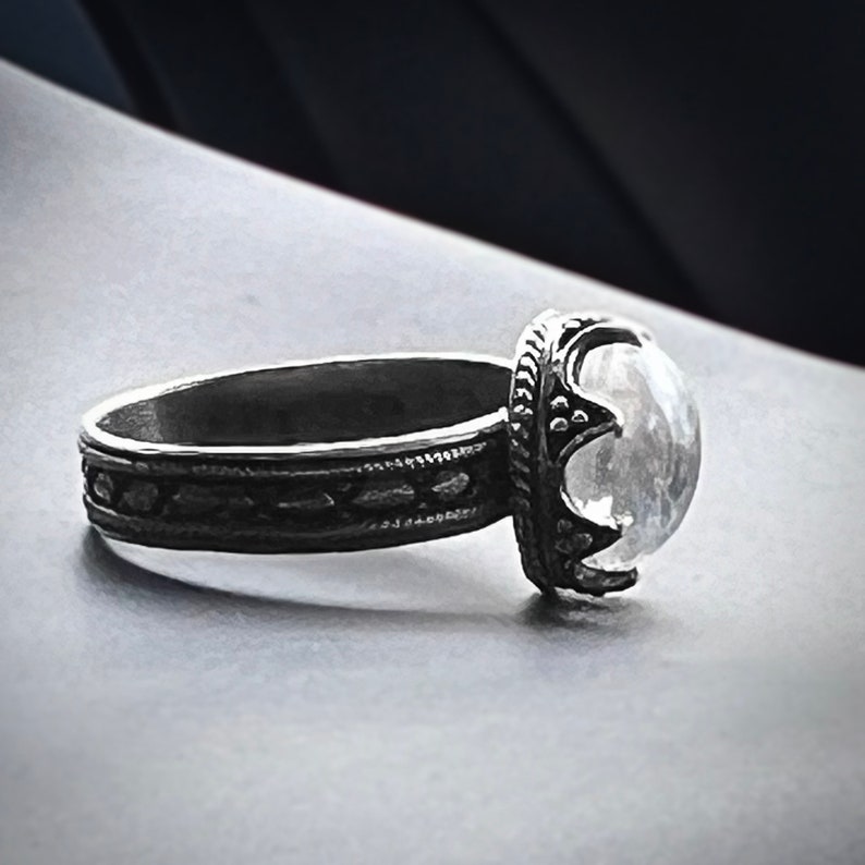 May include: A silver ring with an ornate design and a large, clear gemstone.