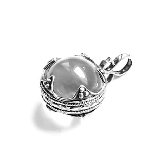 May include: A silver pendant with a round, white gemstone set in a detailed silver frame. The pendant has a loop for attaching to a chain.