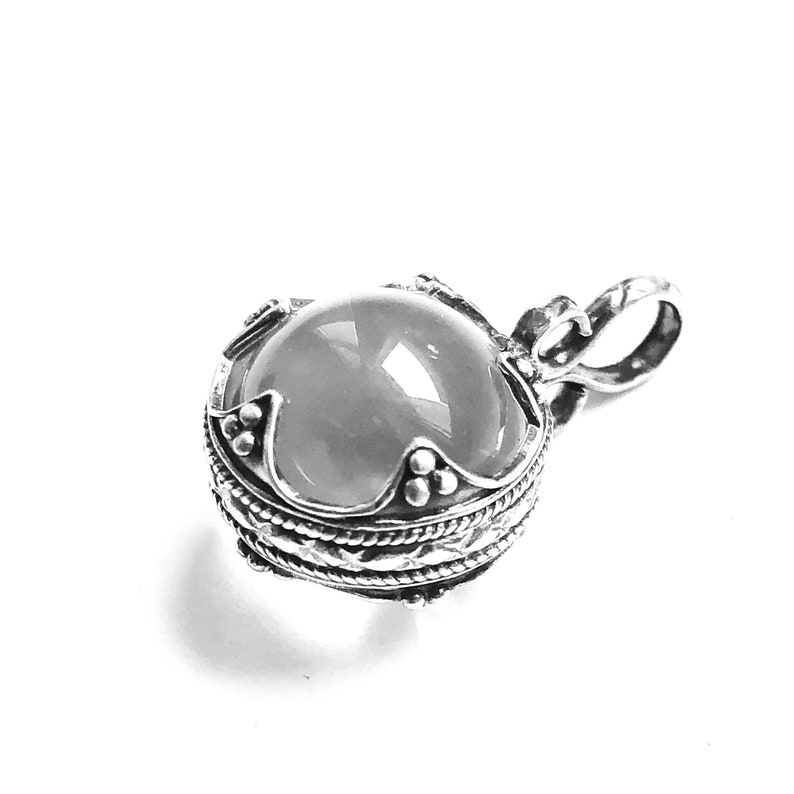 May include: A silver pendant with a round, white gemstone set in a detailed silver frame. The pendant has a loop for attaching to a chain.