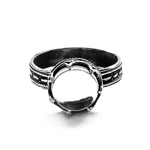 May include: A silver ring with a round bezel setting. The ring has a decorative band with a repeating pattern.