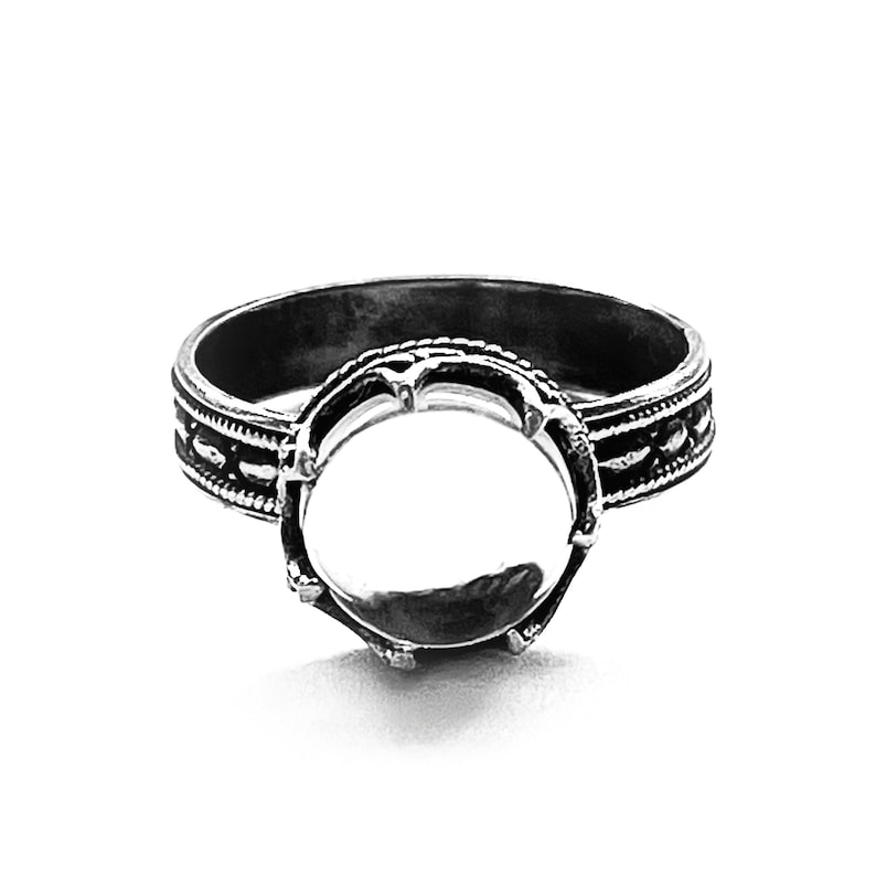 May include: A silver ring with a round bezel setting. The ring has a decorative band with a repeating pattern.