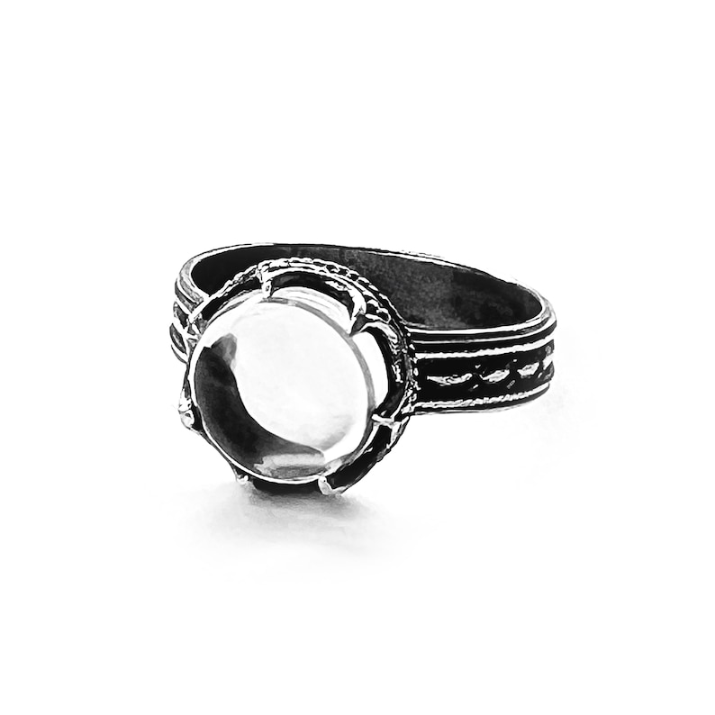 May include: A silver ring with a round, clear stone set in a decorative bezel. The band is detailed with a braided design.