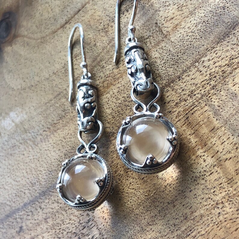 May include: A pair of silver dangle earrings with clear quartz stones. The earrings feature intricate silver designs and are perfect for adding a touch of elegance to any outfit.