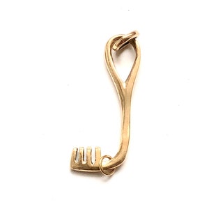 Può includere: Un ciondolo a forma di chiave dorato con una forma organica unica. La chiave ha un design semplice e arrotondato con un piccolo anello in cima per attaccarlo a una catena o un braccialetto.