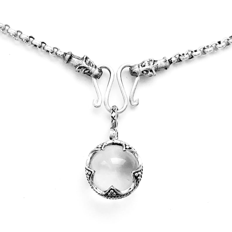 Puede incluir: Un collar de plata con un colgante de cristal transparente. El colgante est&aacute; rodeado por un marco de plata con un dise&ntilde;o floral. El collar tiene dos cierres de plata con cabezas de drag&oacute;n.