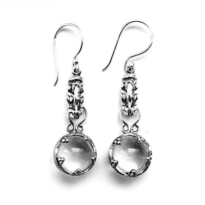 May include: A pair of silver dangle earrings with clear quartz stones. The earrings feature a detailed silver design with a floral motif.