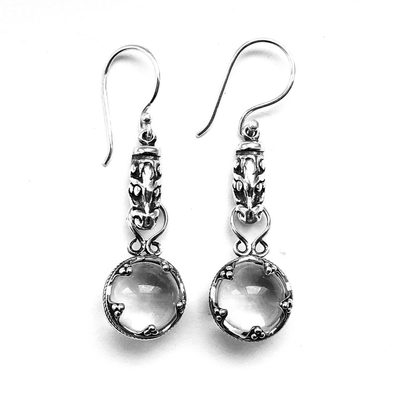 May include: A pair of silver dangle earrings with clear quartz stones. The earrings feature a detailed silver design with a floral motif.