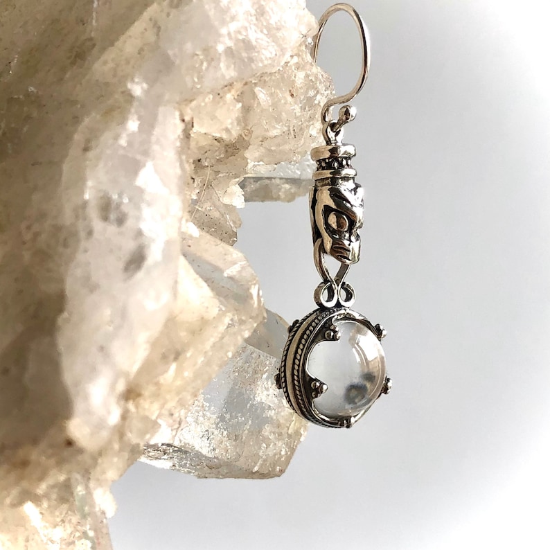 May include: Silver dangle earrings with a clear crystal stone and a detailed silver charm.