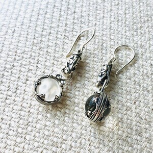 May include: A pair of silver dangle earrings with a white and a black stone. The earrings have a detailed design with intricate silverwork.