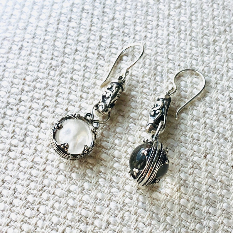 May include: A pair of silver dangle earrings with a white and a black stone. The earrings have a detailed design with intricate silverwork.