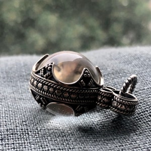 May include: A silver pendant featuring a clear quartz crystal sphere set within an intricate, ornate design. The pendant has a detailed, textured, silver chain.