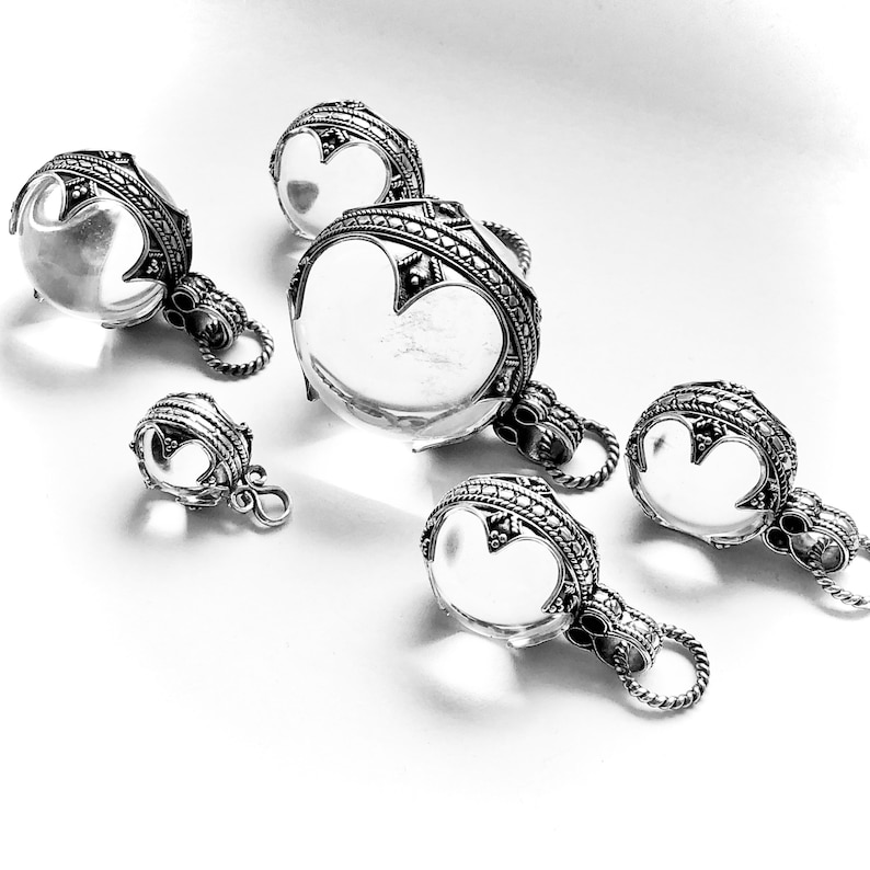 May include: Five silver pendants featuring clear glass orbs. Each pendant has an elaborate design and a loop for attaching to a chain.