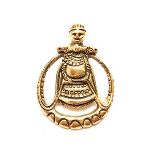 May include: A gold-toned pendant featuring a stylized female figure with a crown and intricate details. The figure is surrounded by a circular frame with a textured design.