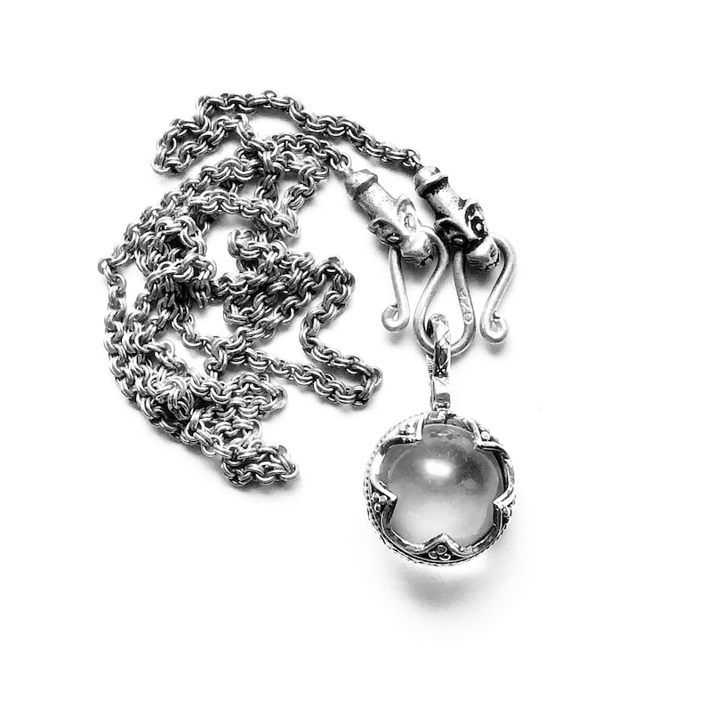 May include: A silver chain necklace with a round pendant featuring a clear stone surrounded by intricate silver detailing.