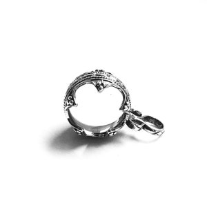 May include: Silver pendant with an ornate, circular design and a small loop for attaching a chain. The pendant has a detailed, intricate pattern.