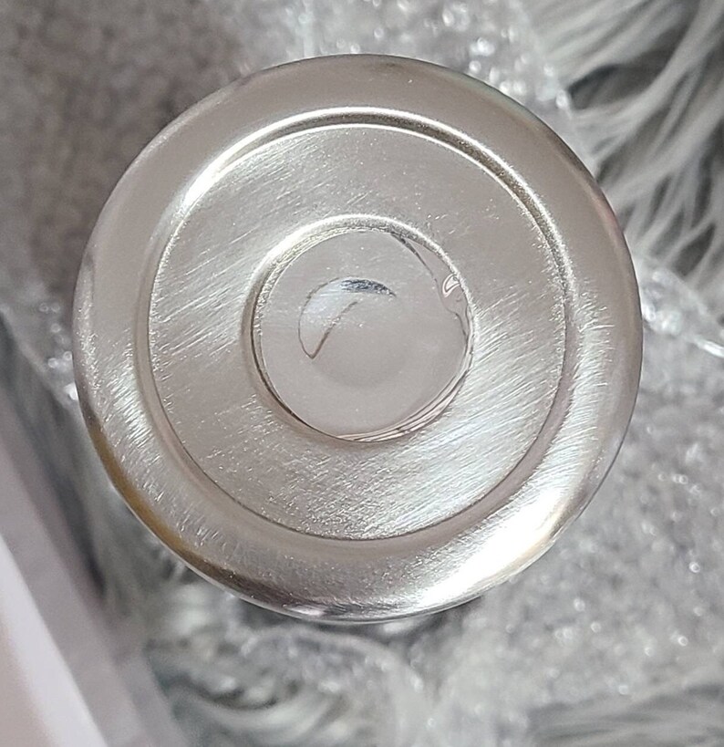 May include: A close-up of a shiny, silver metal lid. The lid features a circular design with concentric rings and a slightly raised centre. The surface has a brushed texture, reflecting light.