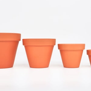 May include: Four terracotta flower pots of varying sizes, arranged from largest to smallest. The pots are all a classic terracotta colour and have a smooth, slightly textured finish.