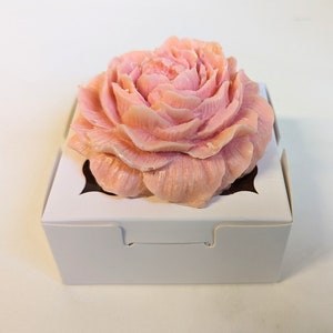 May include: A single pink rose soap in a white box with a cutout for the soap. The soap is shaped like a rose and has a delicate, feminine appearance.